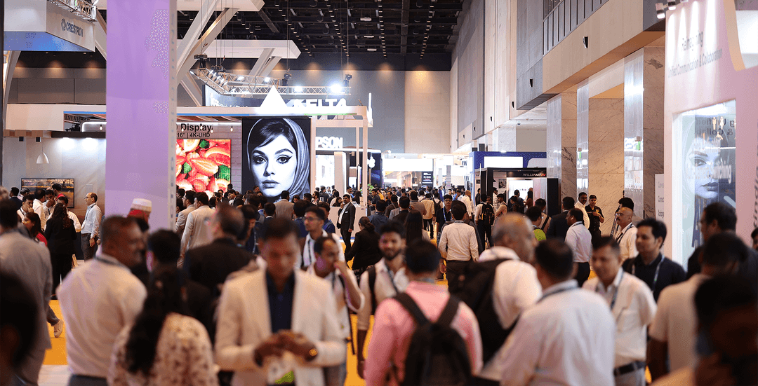 A bustling convention hall filled with people, banners, and digital screens showcasing various technology displays.