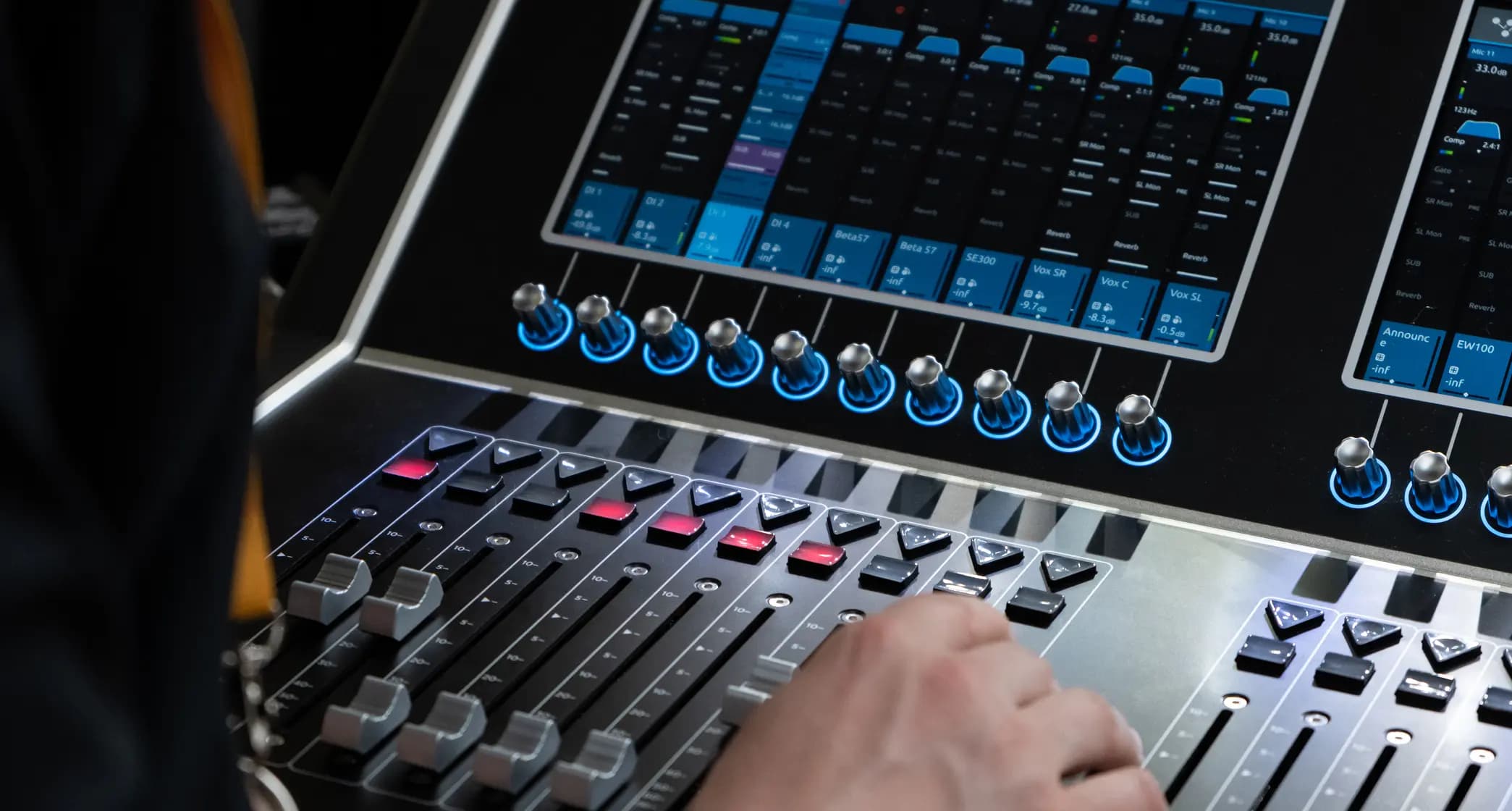 Person operating a sound mixing console with various sliders, buttons, and digital displays.