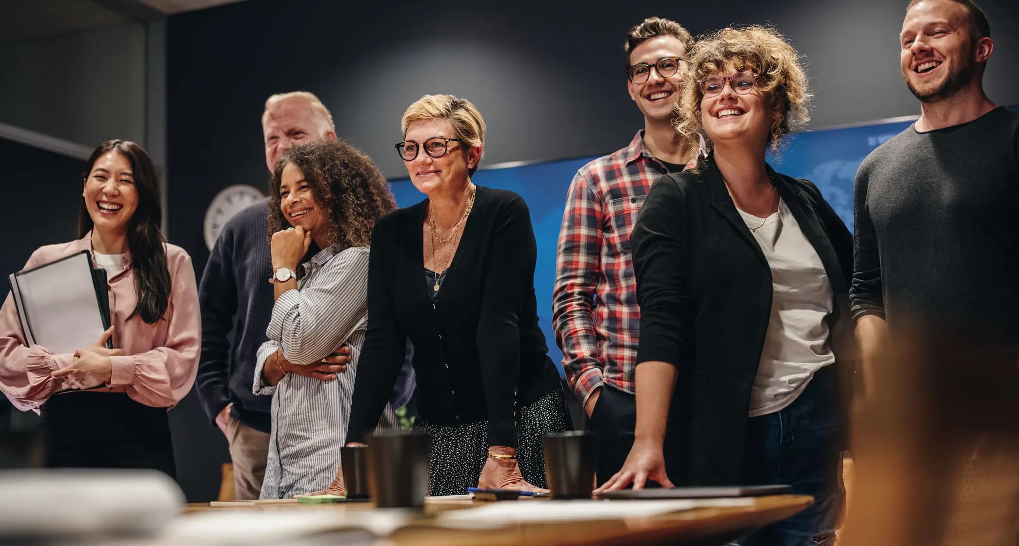 A diverse group of seven people, smiling and standing together in a modern office setting.