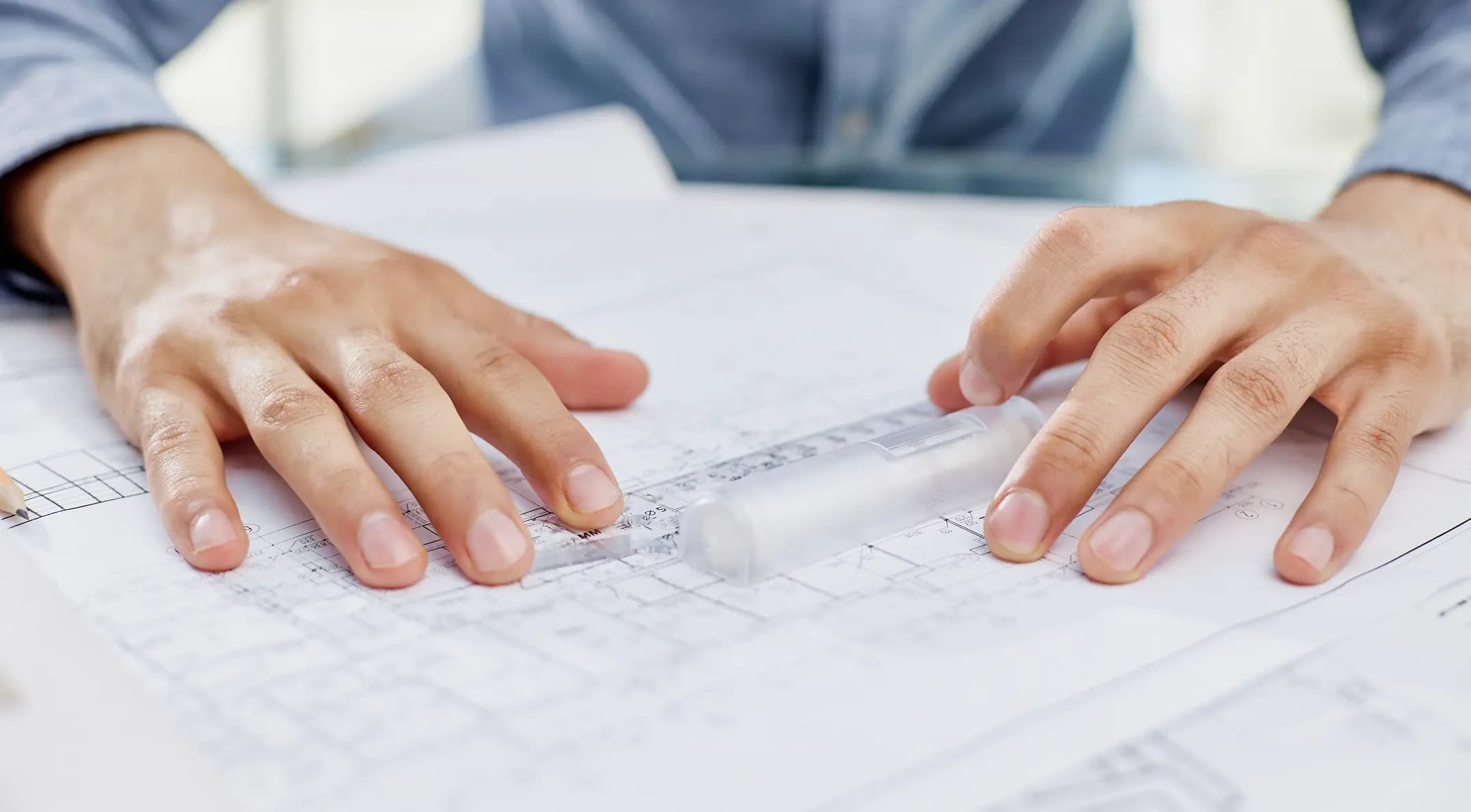 Hands on architectural blueprints with a rolled-up plan, suggesting planning or construction work.