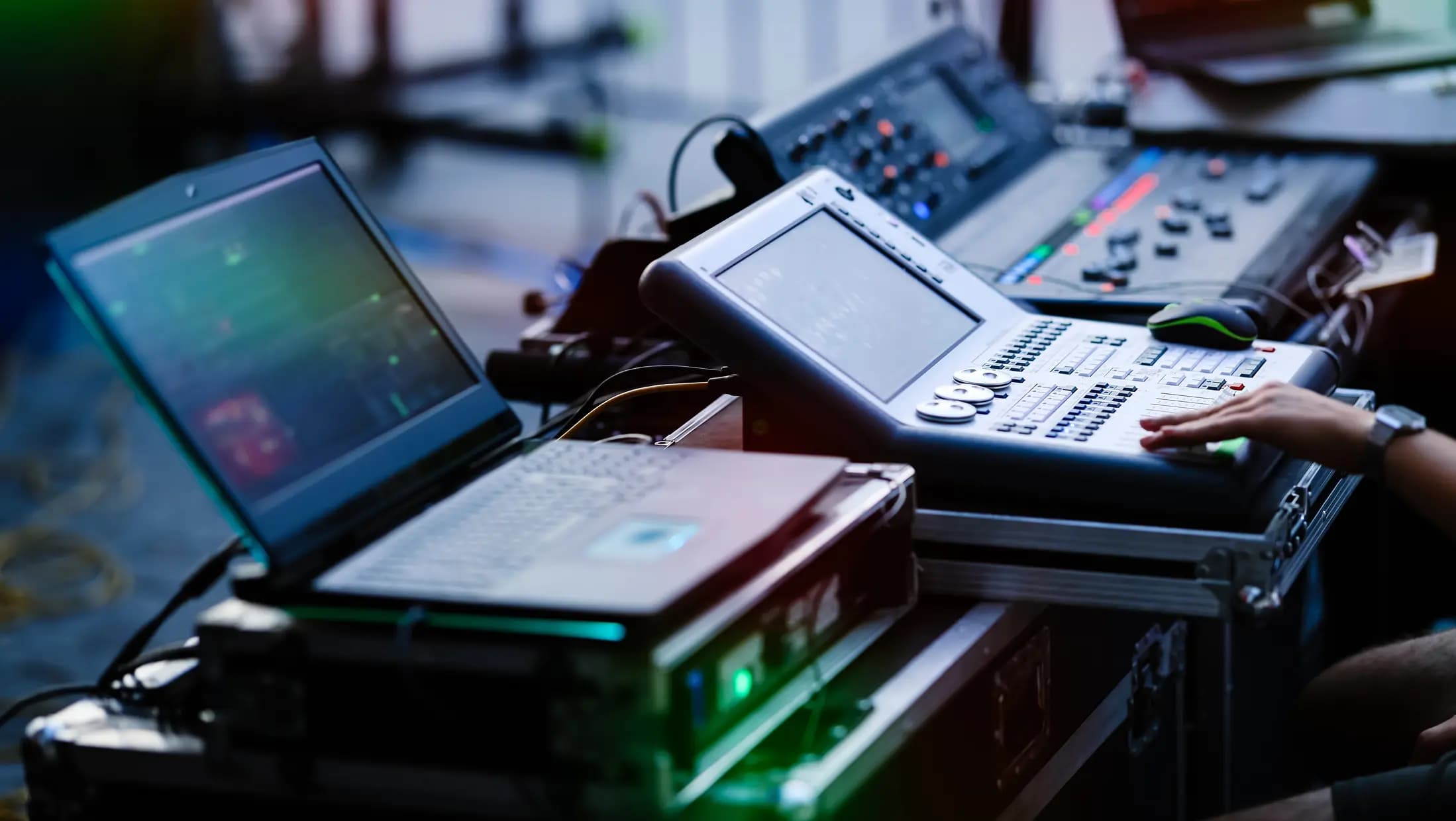 Audio-visual control setup with a laptop, mixing console, and various electronic equipment in a production setting.