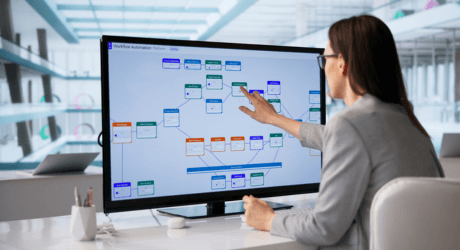 A woman interacts with a digital flowchart on a large monitor in a modern office setting.