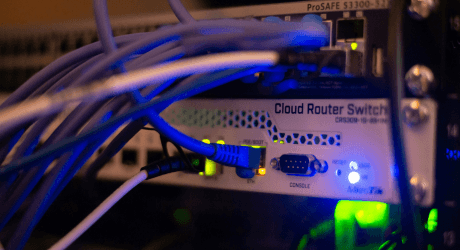 Close-up of a network router with multiple connected cables, LED indicators, and the label "Cloud Router Switch" visible.