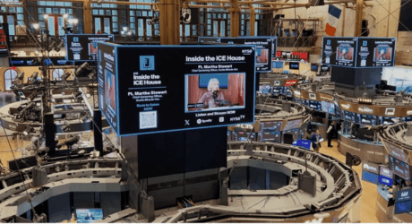 NY Stock Exchange trading floor with large digital screens displaying "Inside the ICE House" featuring a guest speaker, surrounded by trading desks.