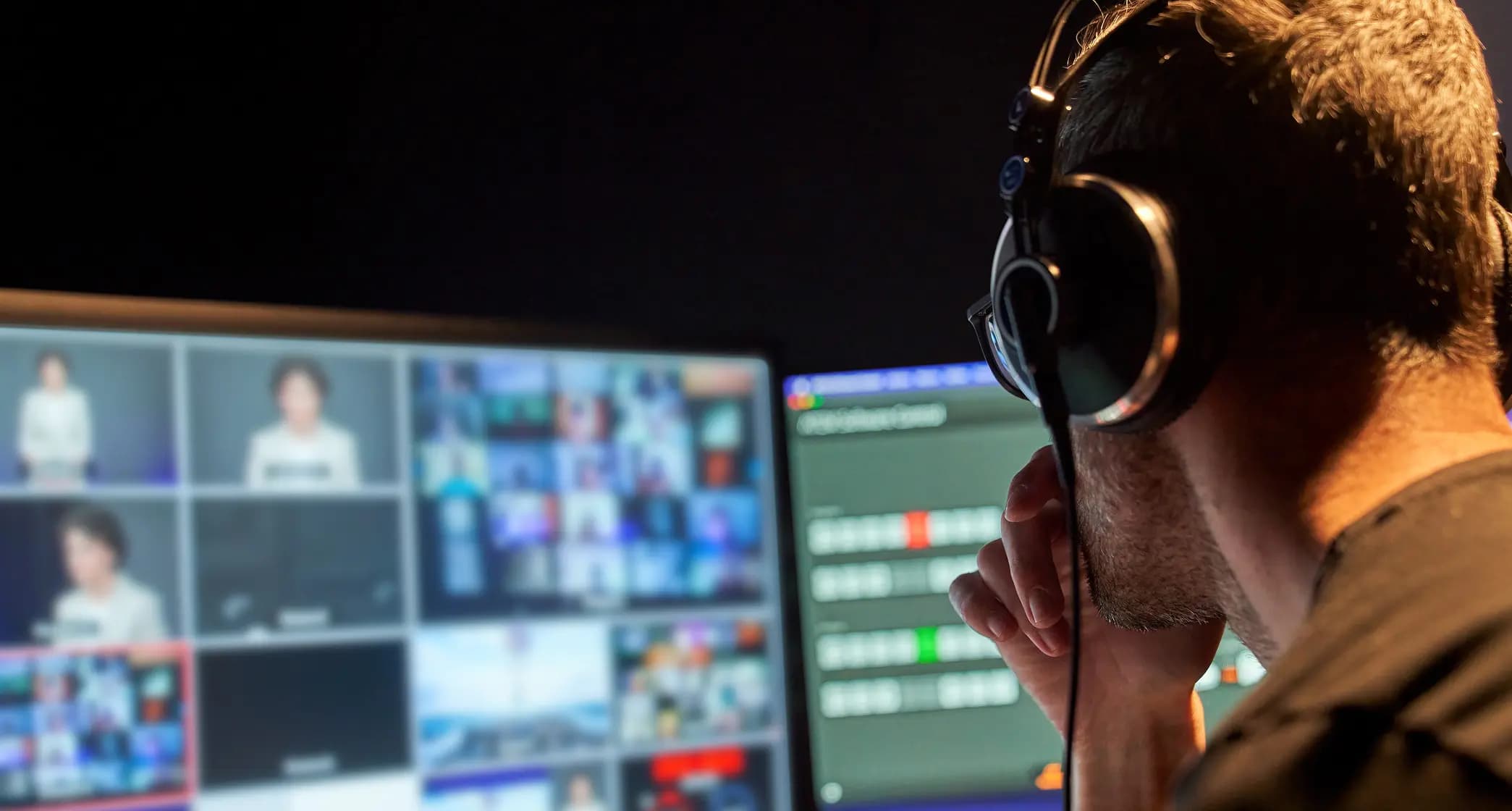 Person in headphones monitors multiple screens in a control room, focused on various media feeds and broadcast controls.