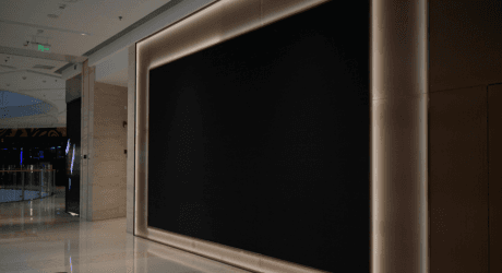 Large black screen on a modern mall wall with surrounding soft lights, reflecting a polished marble floor.