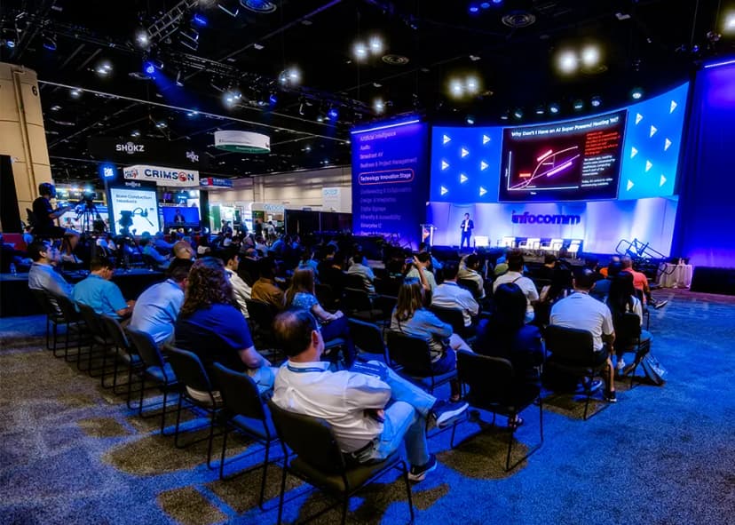 Audience attending a presentation at a conference with a speaker on stage and slides displayed on a large screen.
