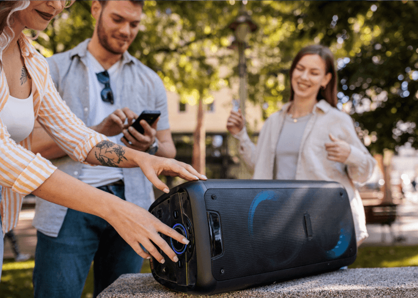 A small group of friends in the park, listening to music from a wireless speaker.